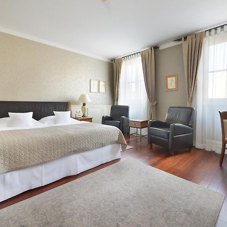 Marrol'S Boutique Hotel Bratislava Exterior foto The photo shows a well-furnished hotel room. The room features a large bed with white linens and a decorative beige coverlet. There are two comfortable armchairs in the corner, along with a small side table. A wooden desk with a chair is also present
