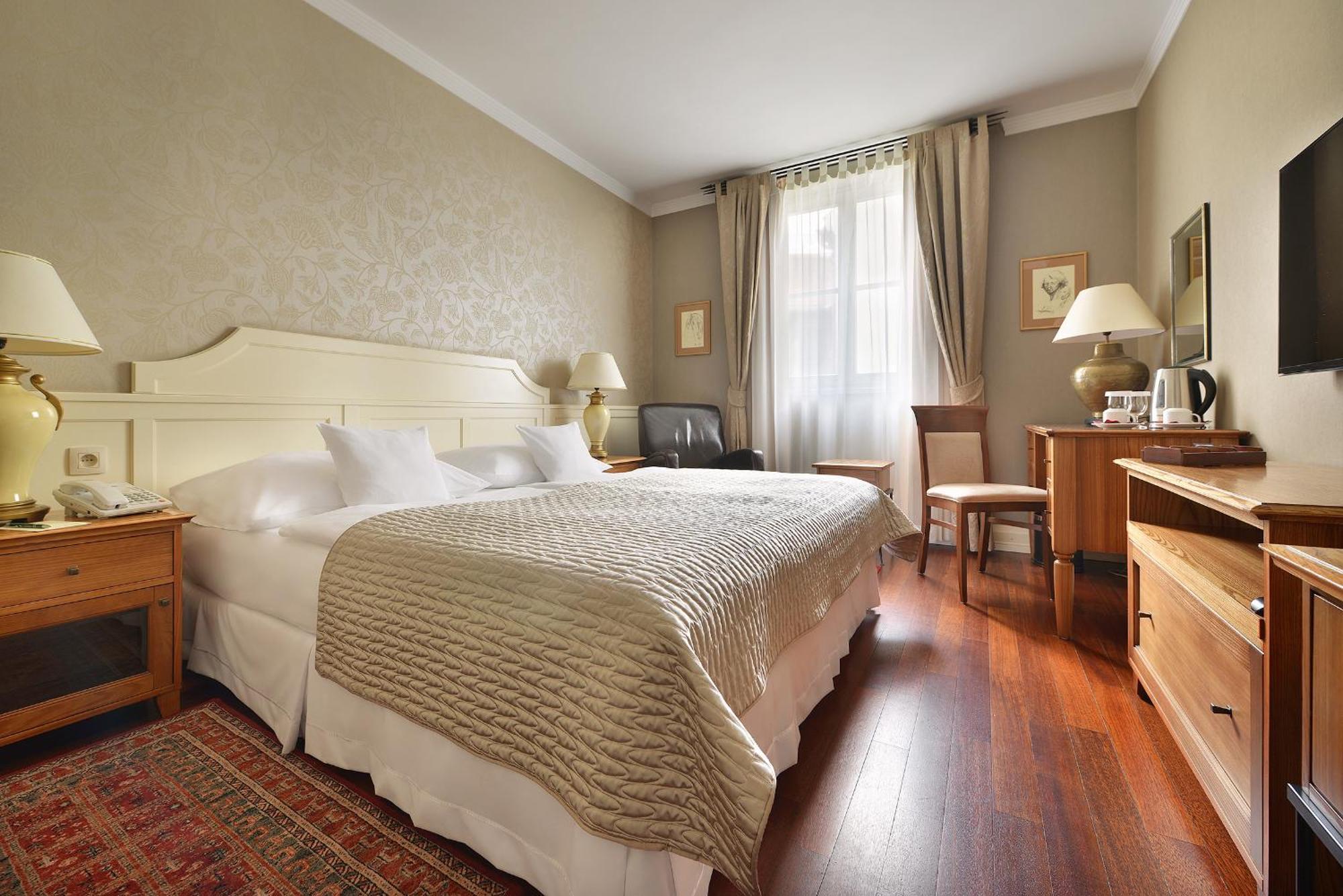 Marrol'S Boutique Hotel Bratislava Quarto foto The photo shows a cozy hotel room with a warm and inviting atmosphere. It features two beds with white linens and a textured beige bedspread. There are bedside lamps on either side of the beds. The room has wooden flooring and is decorated with neutr